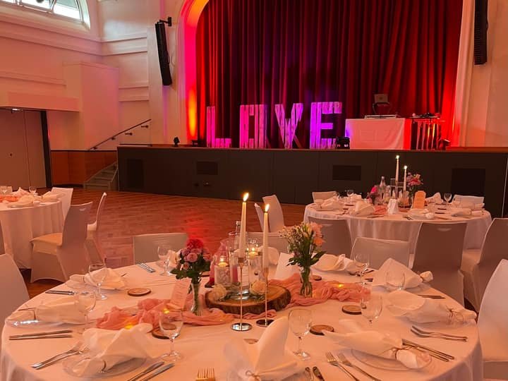 Festsaal mit beleuchtetem Love-Schriftzug und gedeckten Tischen